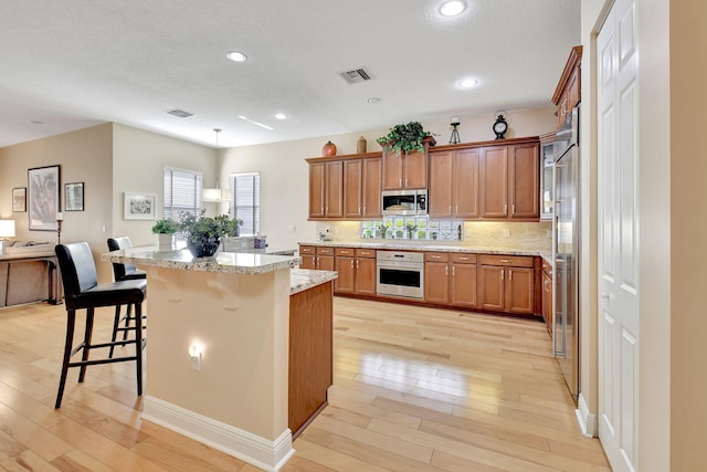 9380 Isles Cay Dr, Delray Beach, FL 33446 - kitchen with appliances with stainless steel finishes, light wood-type flooring, a kitchen breakfast bar, brown cabinets, and light stone countertops