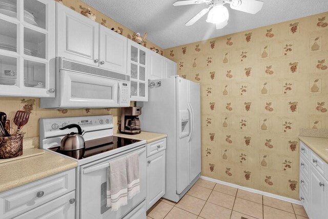 9 Plantation Dr Unit 104, Vero Beach, FL 32966 - kitchen with ceiling fan, white appliances, white cabinets, light tile patterned flooring, and wallpapered walls