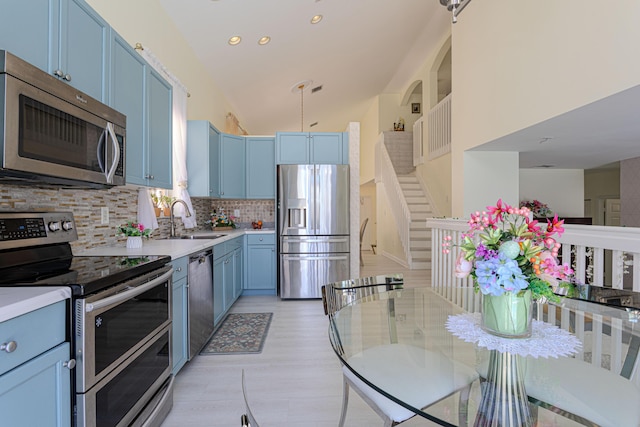 kitchen featuring appliances with stainless steel finishes, blue cabinetry, a sink, tasteful backsplash, and light countertops