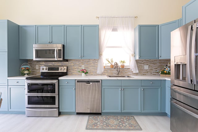 kitchen featuring appliances with stainless steel finishes, a sink, blue cabinets, light wood finished floors, and light countertops