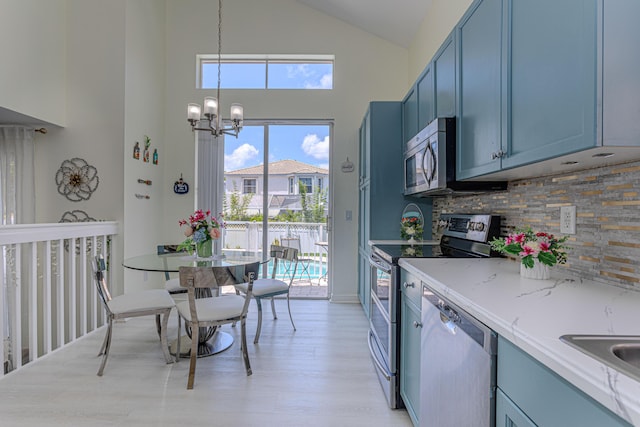 kitchen featuring stainless steel appliances, blue cabinetry, high vaulted ceiling, tasteful backsplash, and a chandelier