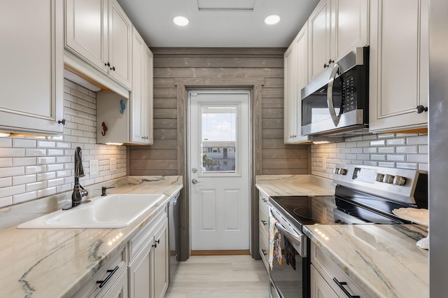 1116 Lake Ter Unit 203, Boynton Beach, FL 33426 - kitchen featuring appliances with stainless steel finishes, decorative backsplash, light stone counters, a sink, and light wood-type flooring