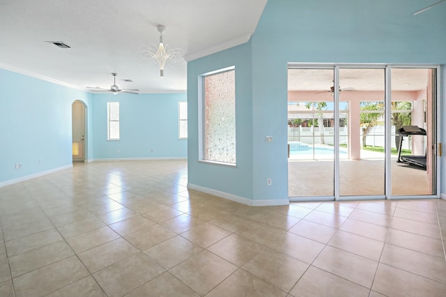 tiled empty room featuring ceiling fan, arched walkways, baseboards, crown molding, and a chandelier