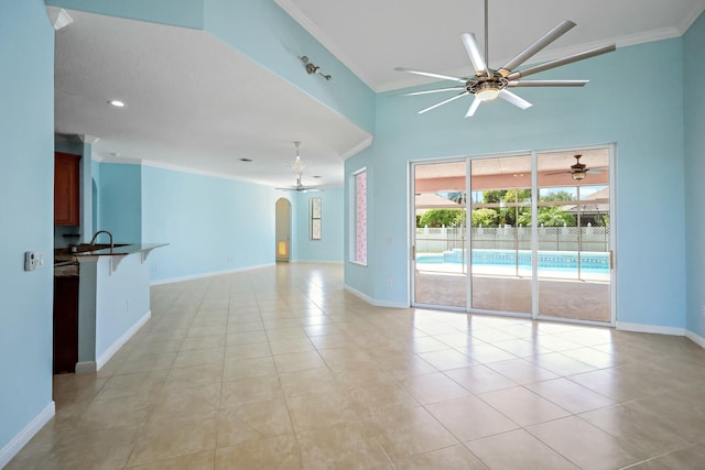 spare room featuring a ceiling fan, crown molding, arched walkways, baseboards, and light tile patterned floors