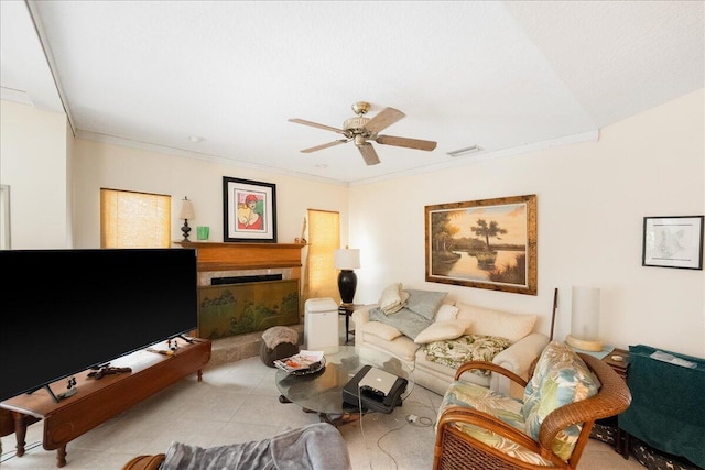 living area featuring crown molding, a fireplace with raised hearth, a ceiling fan, and visible vents