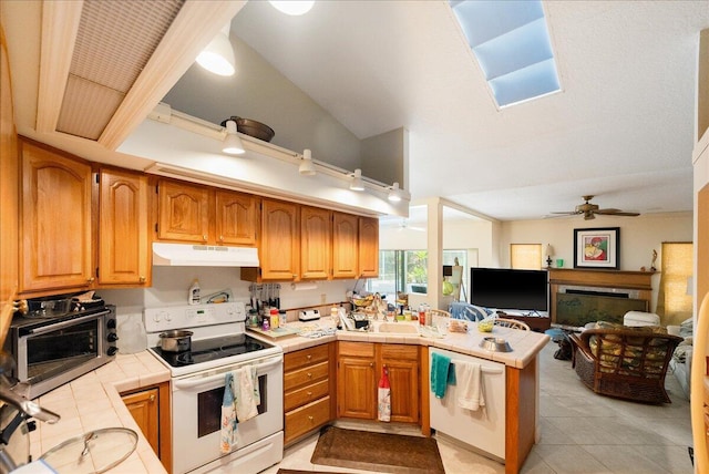 kitchen with a ceiling fan, tile countertops, white appliances, a peninsula, and under cabinet range hood