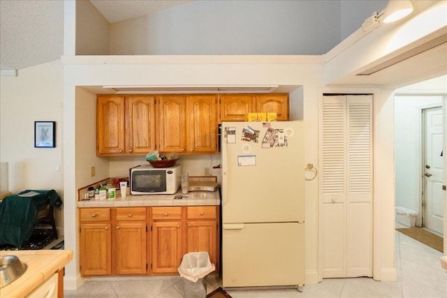 kitchen with brown cabinetry, tile counters, white appliances, and light tile patterned floors