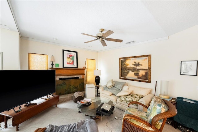 living area featuring tile patterned floors, a tiled fireplace, visible vents, ceiling fan, and crown molding