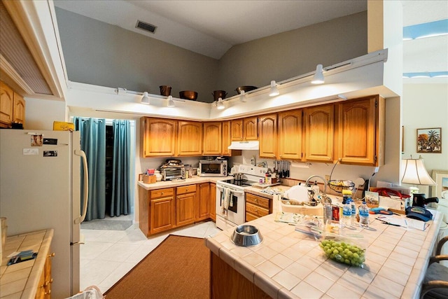 kitchen with high vaulted ceiling, tile counters, white appliances, under cabinet range hood, and visible vents