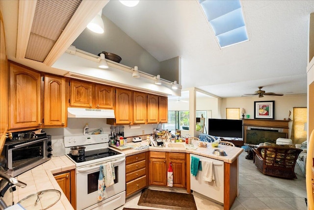 kitchen with tile countertops, white appliances, ceiling fan, a peninsula, and under cabinet range hood