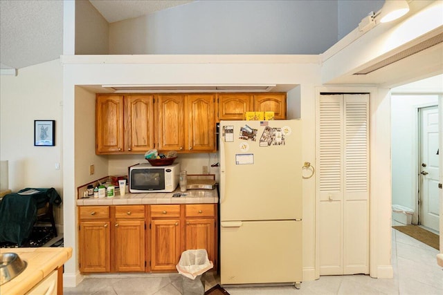 kitchen featuring brown cabinetry, white appliances, and light tile patterned floors