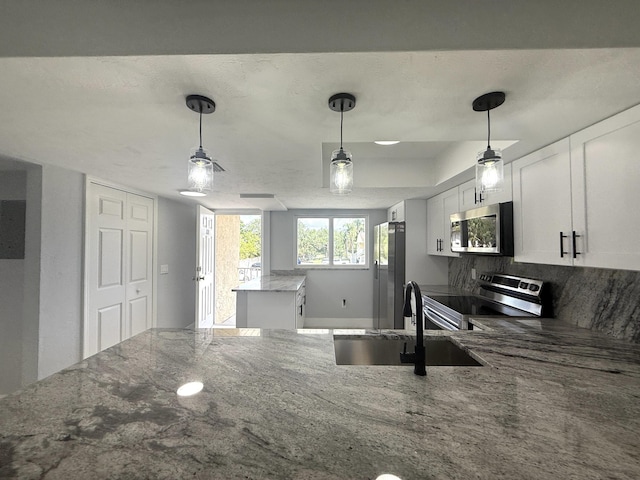 208 Palm Beach Trace Dr, Royal Palm Beach, FL 33411 - kitchen with stainless steel appliances, a sink, stone counters, white cabinetry, and decorative light fixtures