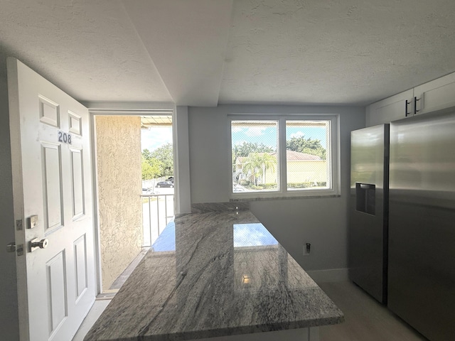 208 Palm Beach Trace Dr, Royal Palm Beach, FL 33411 - kitchen with stainless steel refrigerator with ice dispenser, a textured ceiling, plenty of natural light, dark stone counters, and baseboards