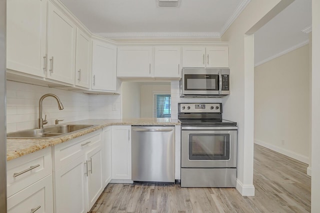 kitchen featuring a sink, crown molding, decorative backsplash, light wood-style flooring, and appliances with stainless steel finishes