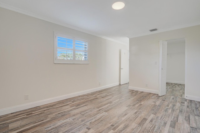 spare room with visible vents, light wood finished floors, baseboards, and ornamental molding