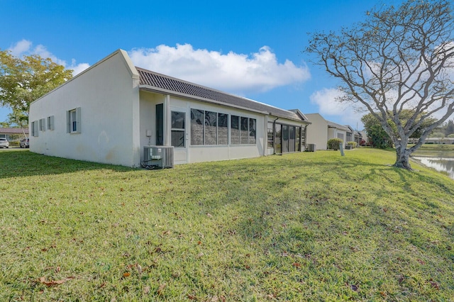 rear view of house featuring central AC, a water view, stucco siding, and a lawn