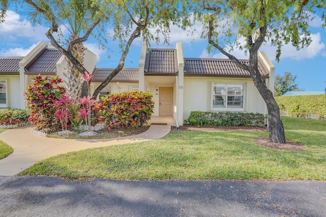 view of front of house featuring a tile roof, a front yard, and stucco siding