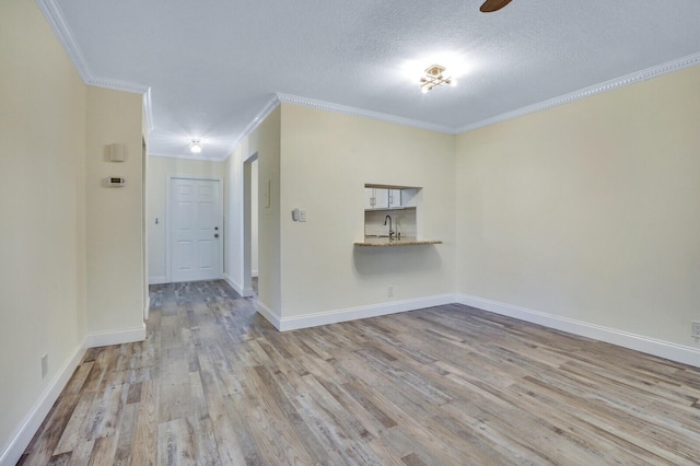 unfurnished room with wood finished floors, ornamental molding, a sink, baseboards, and a textured ceiling