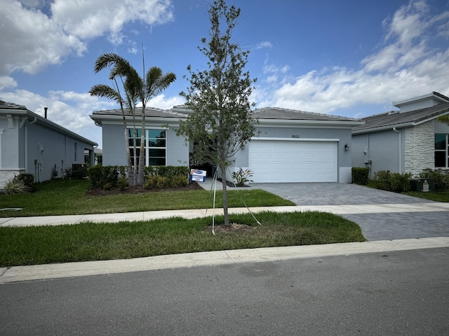 9833 SW Isabelline Dr, Port Saint Lucie, FL 34987 - ranch-style house featuring decorative driveway, stucco siding, an attached garage, central AC, and a front lawn