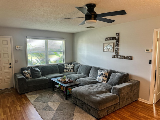living room featuring visible vents, a textured ceiling, a ceiling fan, and dark wood finished floors
