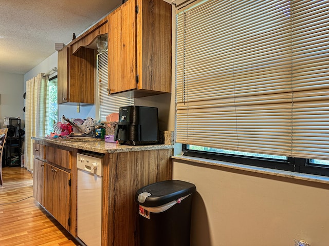 kitchen with brown cabinets, dishwasher, a textured ceiling, and light wood finished floors