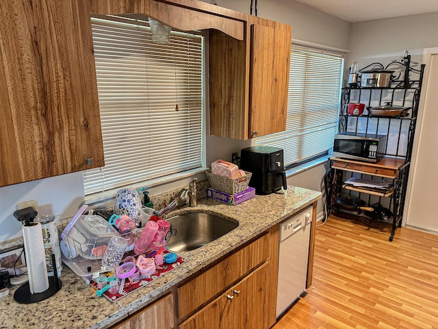 kitchen featuring white dishwasher, a sink, light wood-style floors, brown cabinets, and stainless steel microwave