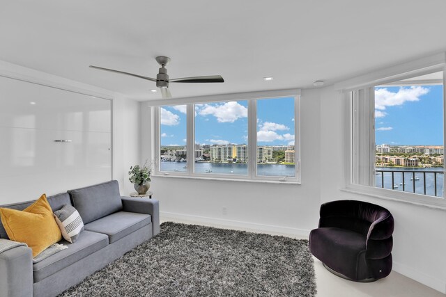 living room with baseboards, a ceiling fan, a water view, and a healthy amount of sunlight