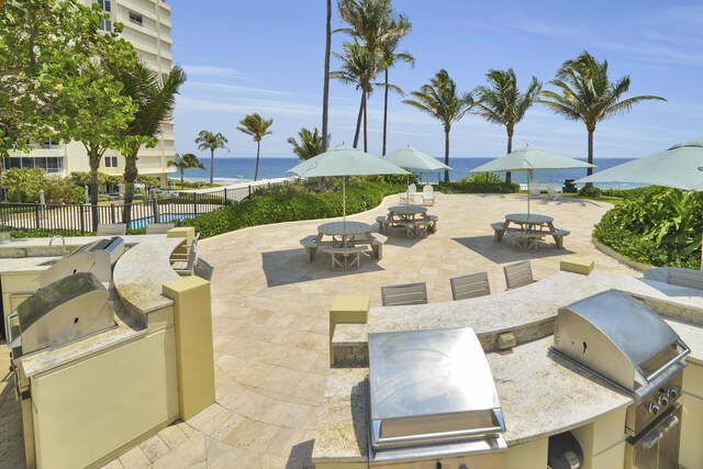 view of patio / terrace featuring a water view, fence, an outdoor kitchen, outdoor dining space, and a grill