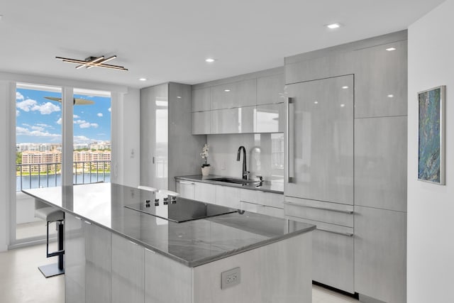 kitchen with modern cabinets, a spacious island, a sink, black electric stovetop, and dark stone counters