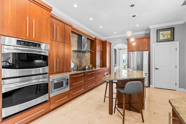 kitchen featuring crown molding, brown cabinetry, wall chimney range hood, and stainless steel appliances