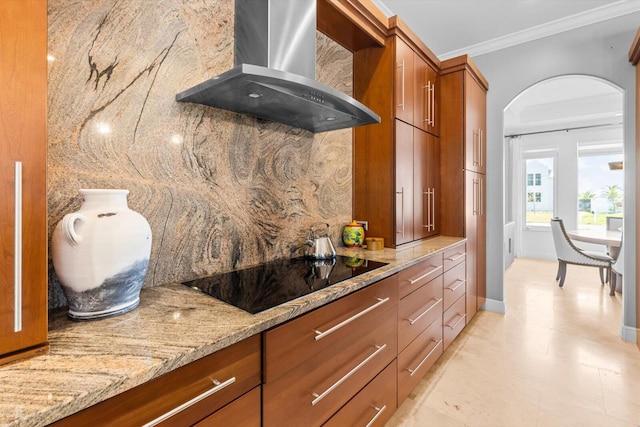 kitchen with light stone countertops, brown cabinets, black electric stovetop, crown molding, and wall chimney range hood