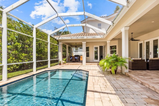 outdoor pool featuring glass enclosure, a ceiling fan, and a patio area