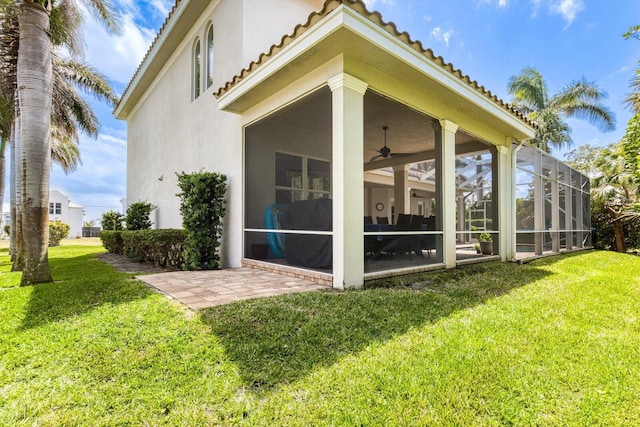 rear view of property with a tile roof, a sunroom, a yard, and stucco siding