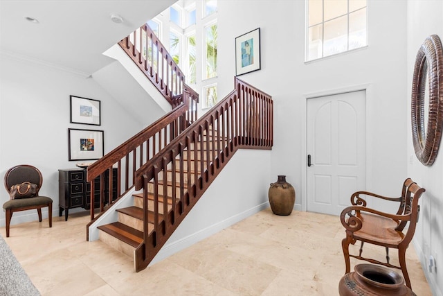 stairway with baseboards, crown molding, and a towering ceiling