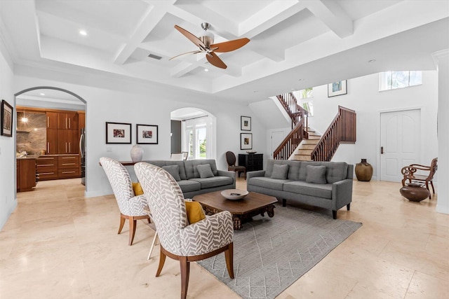 living room with beamed ceiling, stairway, ceiling fan, coffered ceiling, and arched walkways