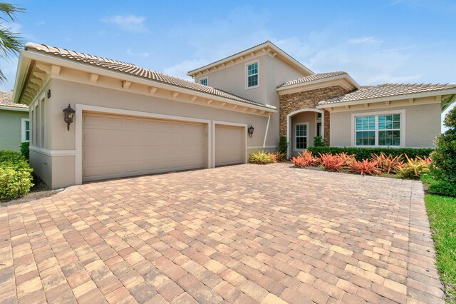 mediterranean / spanish home featuring a tile roof, stucco siding, decorative driveway, and an attached garage