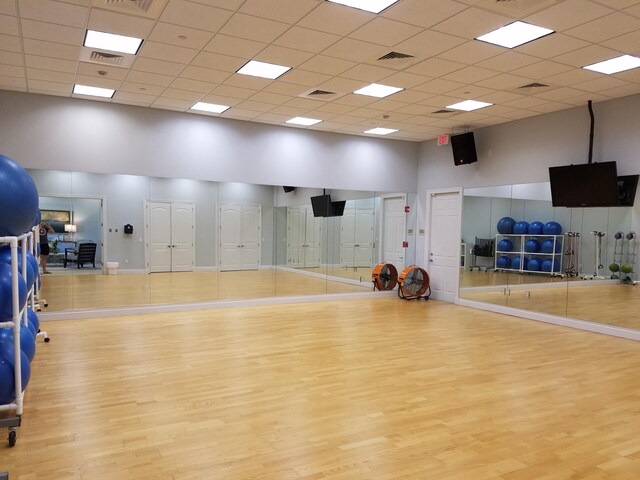 exercise room with wood finished floors, a paneled ceiling, visible vents, and a high ceiling