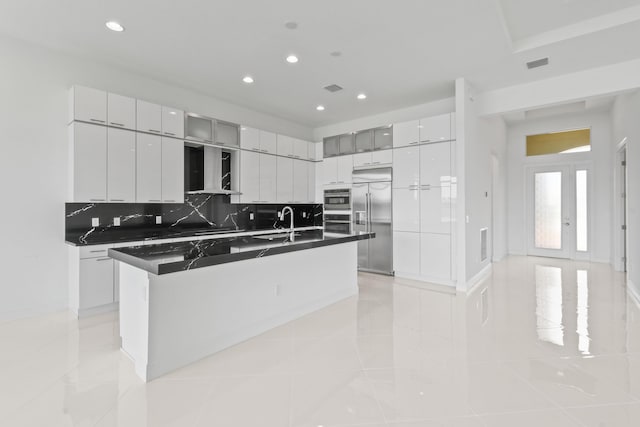 kitchen with stainless steel appliances, wall chimney range hood, dark countertops, backsplash, and a sink
