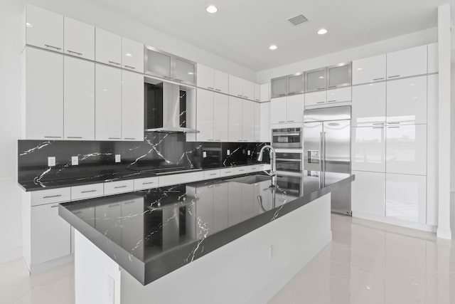 kitchen with wall chimney range hood, decorative backsplash, a sink, dark countertops, and built in fridge