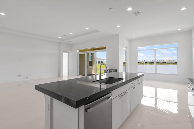 kitchen featuring dark countertops, dishwasher, a sink, open floor plan, and a center island with sink
