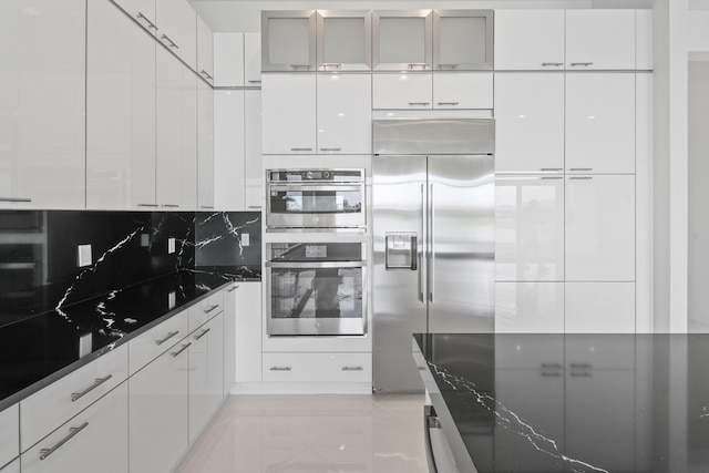 kitchen featuring dark stone counters, modern cabinets, tasteful backsplash, white cabinetry, and appliances with stainless steel finishes