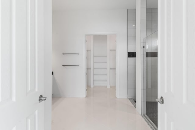 bathroom with a walk in closet, baseboards, tiled shower, and tile patterned flooring
