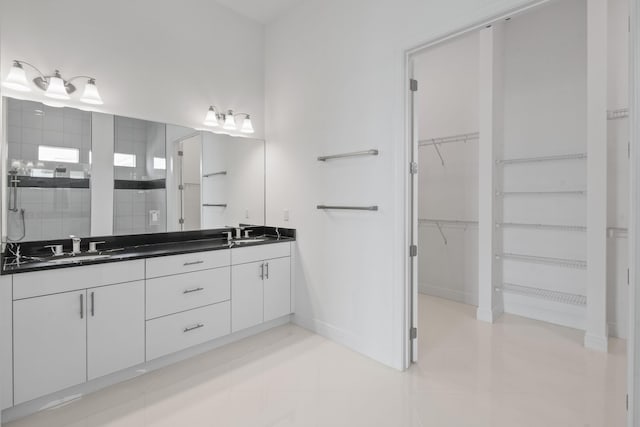 bathroom featuring a sink, tiled shower, double vanity, a walk in closet, and baseboards