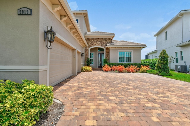 view of front of house featuring stucco siding, decorative driveway, central AC unit, a tile roof, and an attached garage
