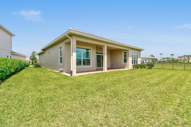rear view of property featuring fence, a patio area, a yard, and stucco siding