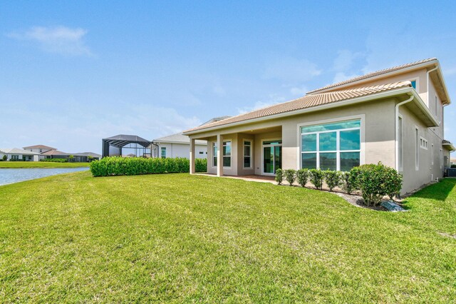 back of property with stucco siding, a yard, a water view, and a tile roof