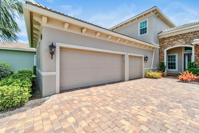 view of front of home with decorative driveway, stucco siding, a tiled roof, and a garage