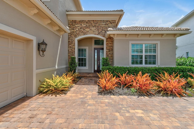 view of exterior entry featuring an attached garage, stucco siding, a tiled roof, and stone siding