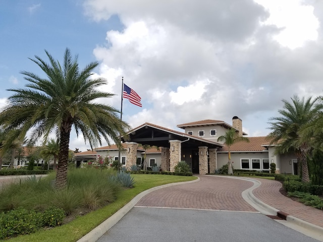 mediterranean / spanish-style house featuring a chimney, curved driveway, stucco siding, and a tiled roof