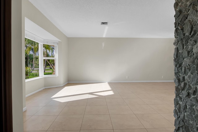 empty room featuring baseboards, visible vents, a textured ceiling, and light tile patterned floors